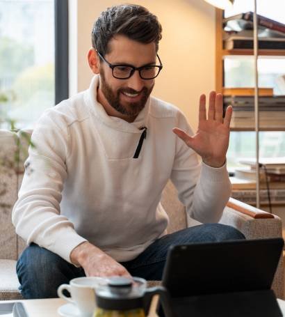 Hombre sentado en su oficina con un té, comenzando una reunión online en su tablet.